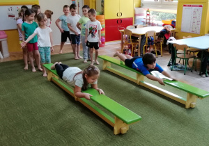 Dzieci pokonują ławeczkę w leżeniu przodem - ćwiczą mięśnie rąk